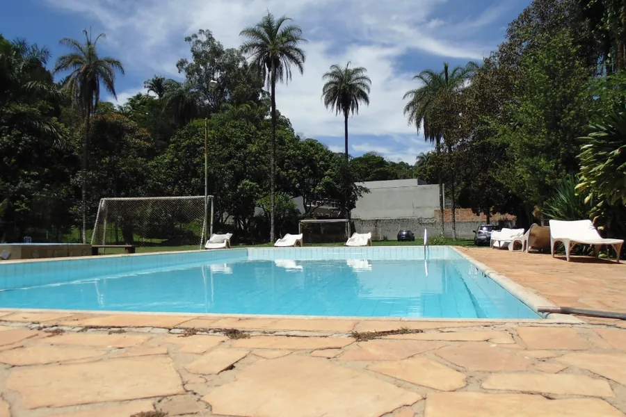Área de piscina cercada de árvores, com campo ao fundo